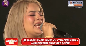 Una mujer de cabello rubio sostiene un micrófono cerca del rostro y llora frente a un fondo negro