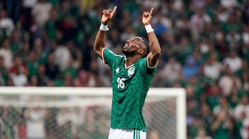 Un jugador de fútbol con la camiseta verde del número 16 alza los brazos y apunta hacia arriba frente a una portería y la tribuna.