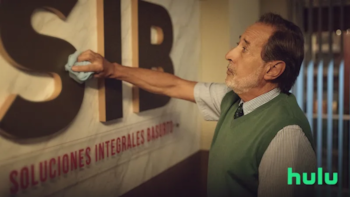 Hombre con chaleco verde y camisa a rayas limpia una letra "S" grande y oscura con un paño azul. Debajo, un cartel con letras rojas dice "SOLUCIONES INTEGRALES BASURTO"