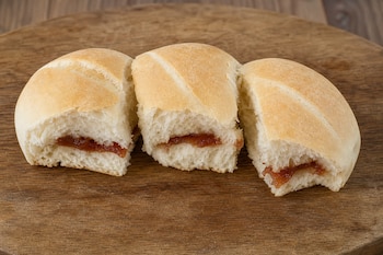 Tres trozos de pan blanco rellenos con una capa de dulce de guayaba sobre una superficie redonda de madera.