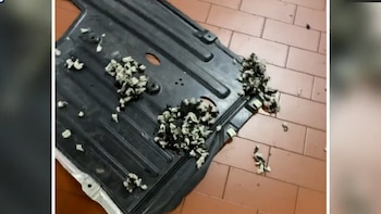 Primer plano de una pieza de coche negra cubierta con trozos de material blanco y oscuro masticado, sobre un suelo de baldosas color salmón