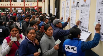 Larguísimas filas de votantes de diversas edades con sus DNI en mano revisan carteles electorales en la pared de un colegio en Perú, asistidos por personal de la ONPE.