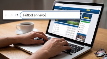 Manos sobre una computadora portátil en cuya pantalla aparece la barra del navegador con el texto Fútbol en vivo, junto a una taza y unos anteojos.