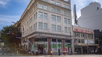 Vista frontal de la Universidad del Salvador en la esquina de Av. Córdoba, con personas caminando en la acera y edificios altos bajo un cielo azul