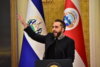Nayib Bukele de traje oscuro habla frente a un atril con la mano alzada, delante de las banderas de El Salvador y Costa Rica