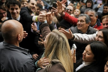 Un hombre calvo de espaldas, una mujer rubia de espaldas y una multitud con manos alzadas y teléfonos móviles en primer plano