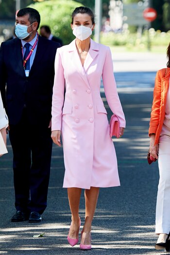 Las mascarillas marcaron el desfile del año 2021, pero ni siquiera su presencia empañaron el día. En una demostración de originalidad, Letizia estrenó un abrigo-vestido de color rosa palo, hombros marcados y escote en forma de pico. Se cerraba al frente con botos vestidos a tono.
Además de un moño de bailarina muy cómodo, lució un bolso rosa de Magrit y zapatos a juego. El punto de color lo pusieron los pendientes, de cuarzo verde y rubíes firmados por Tous.
