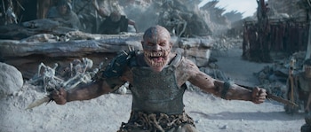 Baraka, una criatura humanoide pálida con rayas azules, boca llena de dientes afilados y garras en los antebrazos, empuña dos cuchillas. Está en un entorno desértico