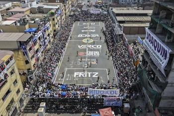 Vista aérea de una calle convertida en cancha de fútbol, repleta de espectadores a los lados y en edificios, con jugadores en el campo