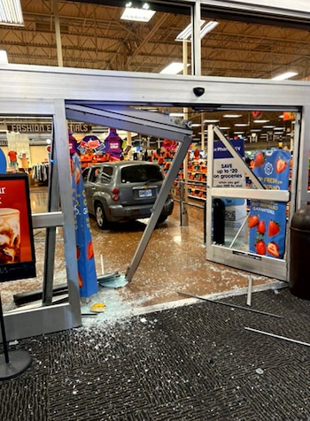 Un automóvil gris está en el interior de un supermercado detrás de una estructura metálica dañada y vidrios rotos en el suelo