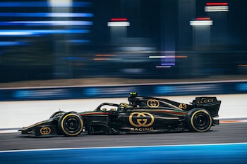 Coche de Fórmula 1 Alpine negro y dorado con logos de Gucci y el número 43, corriendo en una pista oscura con luces de neón azules y rojas borrosas.