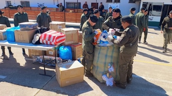 Varios efectivos uniformados con boina negra examinan cajas de cartón, bolsas y un saco grande con juguetes sobre mesas y el suelo