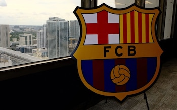 Un escudo grande del FC Barcelona en primer plano, con el horizonte de la ciudad de Miami visible a través de una ventana al fondo