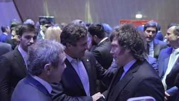 Javier Milei estrecha la mano de un hombre en traje rodeado por otros asistentes en un evento en un salón iluminado