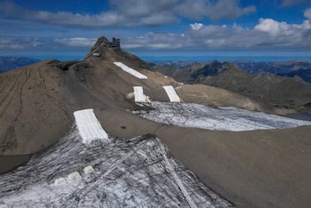 Vista aérea de una cumbre montañosa rocosa con nieve, un edificio en la cima y varias lonas blancas rectangulares sobre el terreno