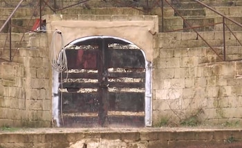 Una puerta doble de madera oscura bajo un arco en un muro de bloques de piedra, con un cable enrollado a la izquierda