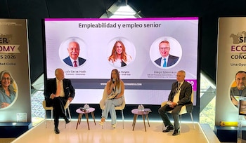 Tres ponentes se encuentran sentados en un escenario frente a una pantalla gigante con fotos y textos explicativos