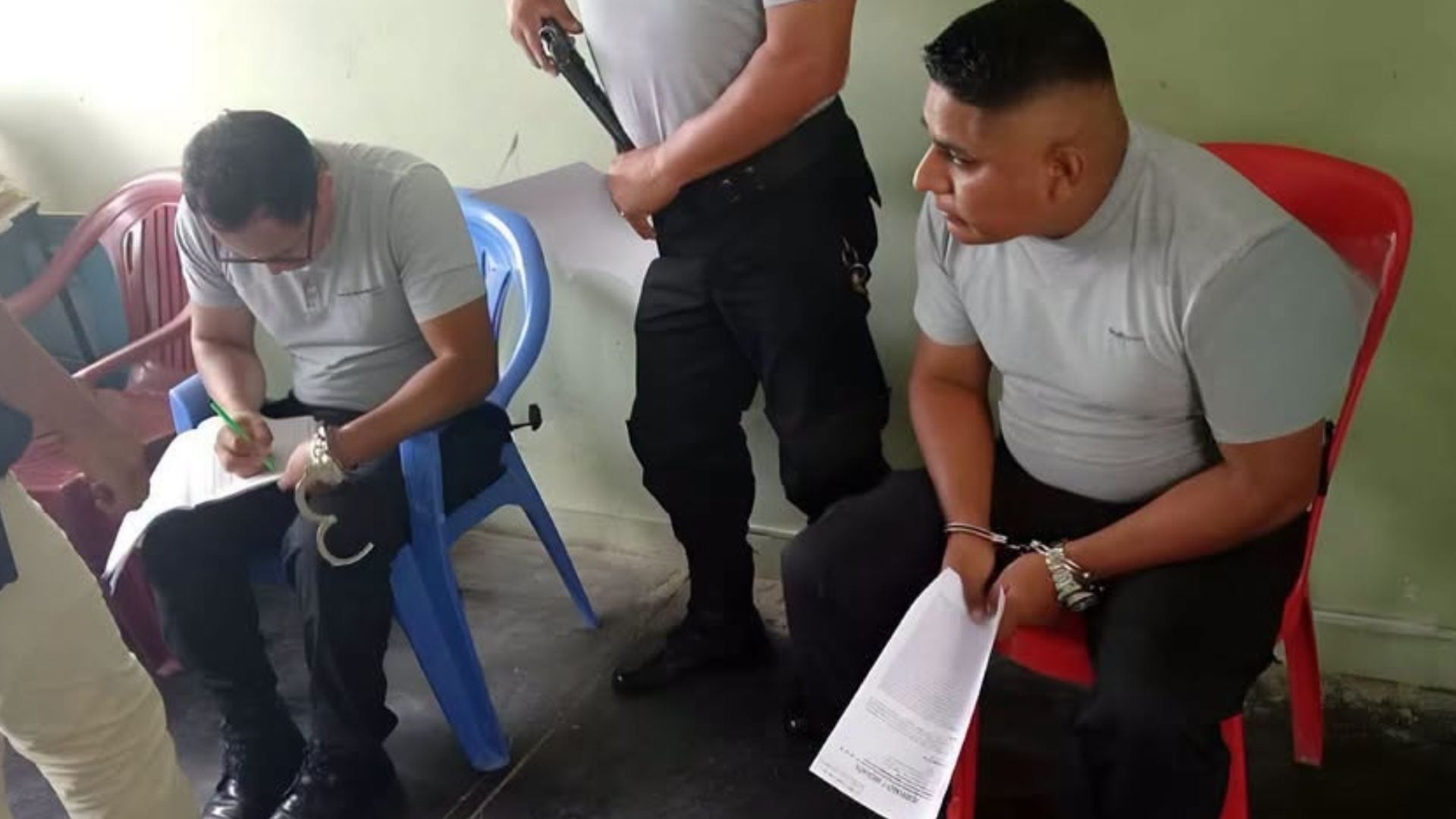 Dos agentes policiales permanecen esposados y firman documentos tras ser detenidos por el presunto cobro de una coima en Piura. (PNP)