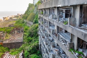 Vista aérea de edificios de hormigón abandonados y cubiertos de vegetación en la isla Hashima, Japón, con ruinas industriales y el mar de fondo bajo un cielo claro