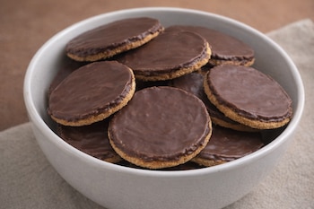 Un primer plano de un bol gris claro lleno de galletas redondas con base de galleta y una capa gruesa de chocolate oscuro.