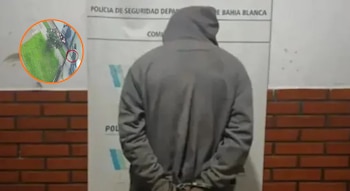 Persona de espaldas con buzo gris y capucha puesta, con las manos esposadas detrás, y un recuadro circular con una grabación de seguridad
