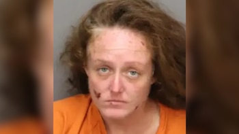 Fotografía de ficha policial de una mujer con cabello castaño y camiseta naranja frente a un fondo gris