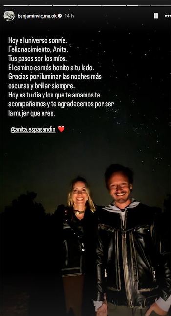 Hombre y mujer sonrientes, tomados de la mano por la noche. Él viste chaqueta de cuero y capucha clara; ella chaqueta de cuero oscura. Cielo con estrellas y árboles
