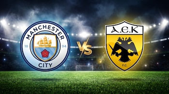 Escudos de Manchester City y AEK Atenas con las letras VS en dorado en el centro, sobre césped y un estadio iluminado de noche.