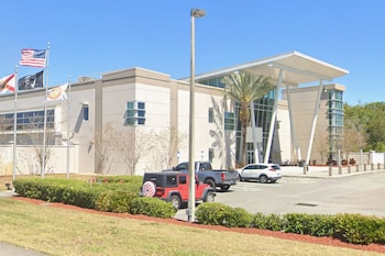 Fachada de un edificio moderno con banderas de Estados Unidos y Florida, vehículos estacionados al frente y una palmera