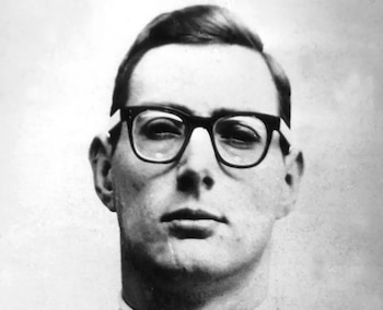 Primer plano en blanco y negro de Bruce Reynolds, un hombre con gafas de montura oscura y cabello peinado hacia atrás, mirando al frente