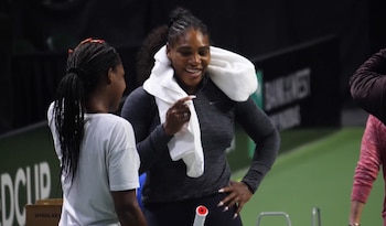 Serena Williams con una toalla blanca al cuello y Coco Gauff de espaldas conversan en una cancha de tenis oscura con raqueta visible