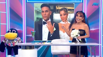 Magaly Medina, vestida de novia negra con velo y un ramo blanco, sonríe y muestra un anillo frente a una pantalla con Christian Domínguez y Karla Tarazona.