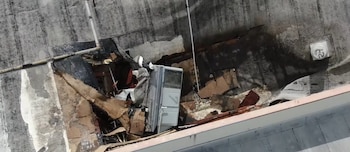Vista aérea de un techo gris con una sección colapsada que muestra escombros, una unidad de aire acondicionado y tuberías. La superficie del techo está húmeda