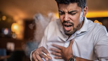 Mid adult African American man smoking a cigarette in the bar and coughing.
