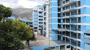 Conjunto de edificios universitarios de varios pisos, azules y blancos, con ventanas y balcones. Se observan personas, árboles y montañas en el fondo
