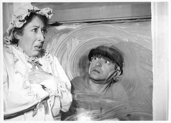 Primer plano en blanco y negro de Nelly Láinez con un vestido de encaje y expresión asustada, y Carlitos Balá con casco mirando a través de una ventana empañada con círculos