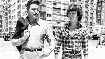 Fotografía en blanco y negro de dos hombres que caminan por la calle ante varios edificios de departamentos
