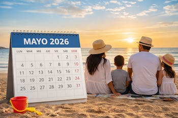 Vista trasera de una familia (hombre, mujer, niño, niña) sentada en una playa mirando el atardecer, con un calendario de Mayo 2026 y juguetes de playa en primer plano.