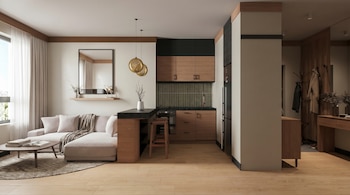 Moderna cocina compacta con gabinetes de madera y azulejos verdes, integrada con una sala de estar que tiene un sofá beige, mesa y ventana grande.