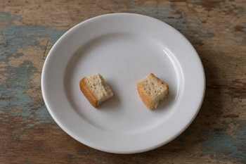 Un plato blanco de cerámica con dos pequeños pedazos de pan sobre una mesa de madera desgastada.