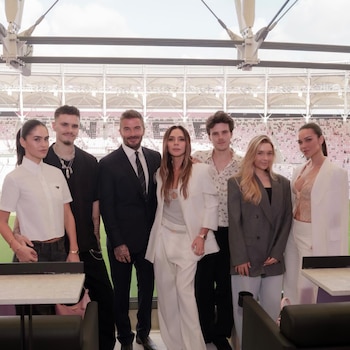 Seis personas, incluyendo a David, Victoria y Brooklyn Beckham, posan sonriendo en un palco de estadio con asientos vacíos en el fondo