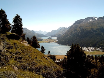 Colina con árboles y arbustos en primer plano frente a un valle con lagos, caseríos y montañas en el horizonte bajo la luz diurna