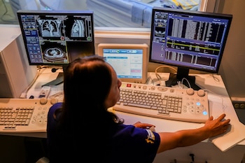 Una persona frente a tres monitores con tomografías médicas y datos de pacientes utiliza un teclado especializado y un ratón