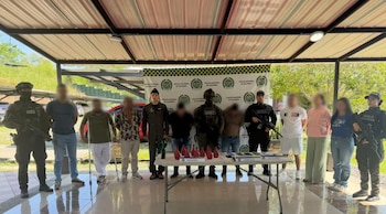 Efectivos policiales uniformados custodian a civiles junto a una mesa con frascos rojos, teléfonos móviles y equipos portátiles