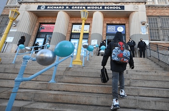 Vista desde abajo de un estudiante de espaldas subiendo escaleras de piedra hacia la entrada de la Escuela Richard R. Green con globos y una farola amarilla