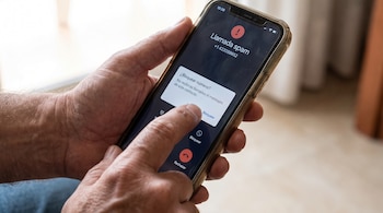 Unas manos sostienen un teléfono móvil cuya pantalla muestra la notificación de una llamada spam y la opción de bloquear el número.