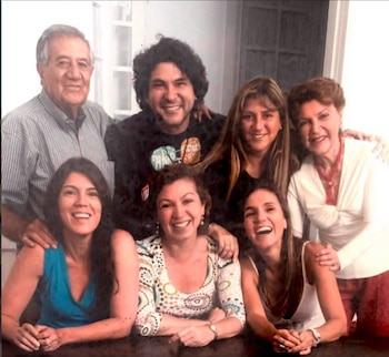 Un grupo de siete personas posa sonriente frente a la cámara alrededor de una mesa de madera en el interior de una vivienda