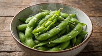 Primer plano de un tazón de edamame verde humeante, salpicado con cristales de sal gruesa, sobre una superficie de madera rústica.