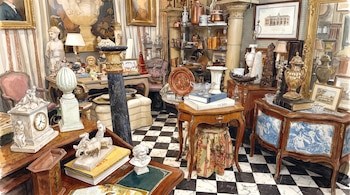 Ilustración en acuarela de una estancia con muebles de madera, esculturas, vasijas, cuadros y un suelo de baldosas blancas y negras.
