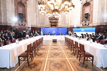 Salón de convenciones con un gran candelabro dorado, mesas largas y blancas dispuestas para asistentes, un panel de oradores en el fondo, y suelo con mosaicos ornamentados